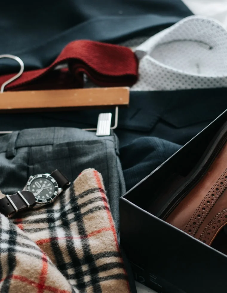 Traje social masculino montado pe&ccedil;a a pe&ccedil;a: palet&oacute; azul-marinho em cabide de madeira, camisa de poa, gravata de tric&ocirc; bord&ocirc;, cal&ccedil;a cinza, rel&oacute;gio e sapatos brogue de couro marrom